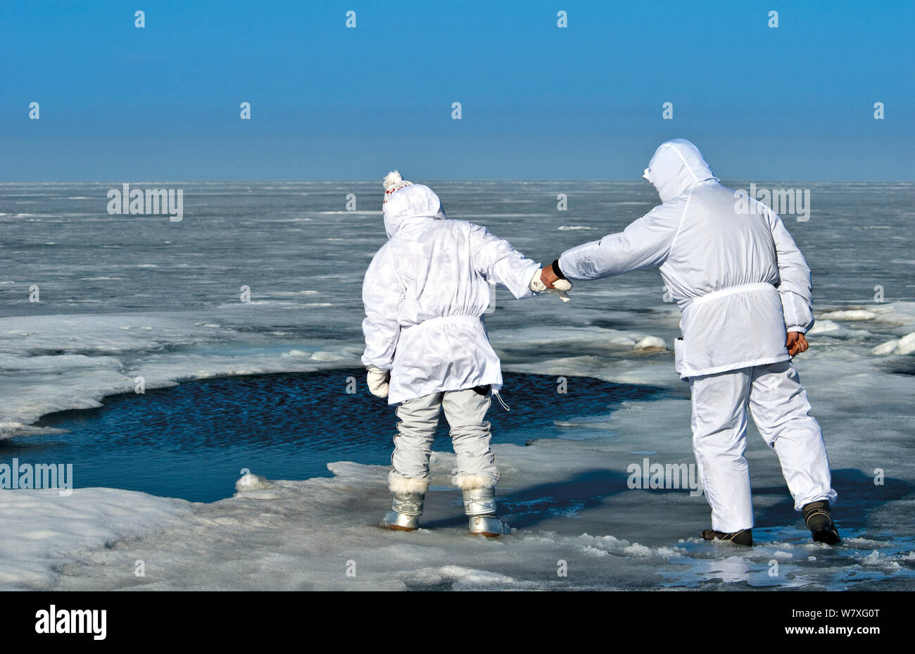 Persone che guardano il foro nel ghiaccio utilizzato da Baikal guarnizioni (Pusa sibirica) per la respirazione. Lago Baikal, Russia, aprile 2009. Foto Stock