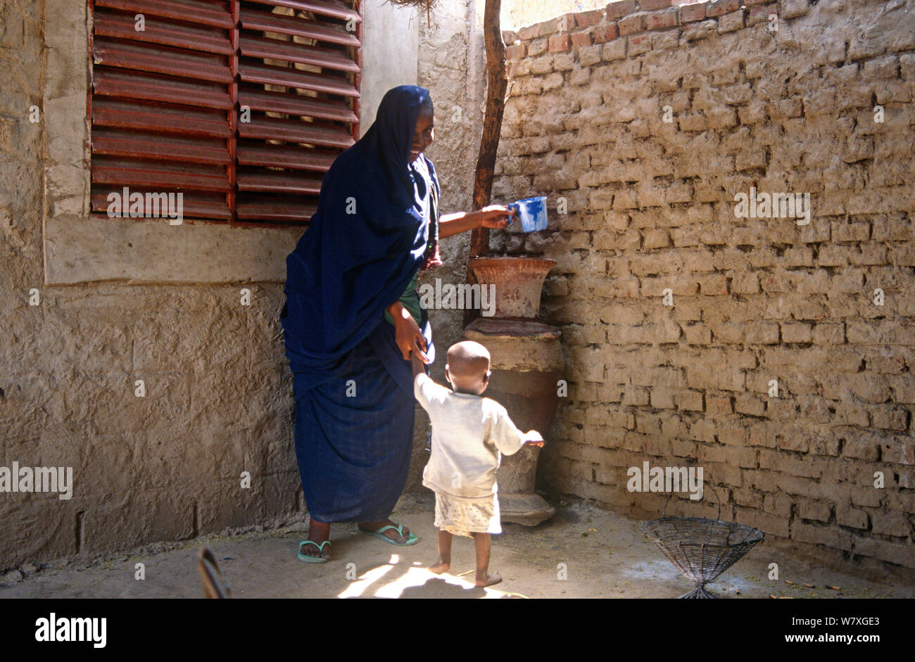 La madre e il bambino beve acqua immagazzinata nel vaso di terracotta. N&#39;Djamena, Ciad, 2002-2003. Foto Stock