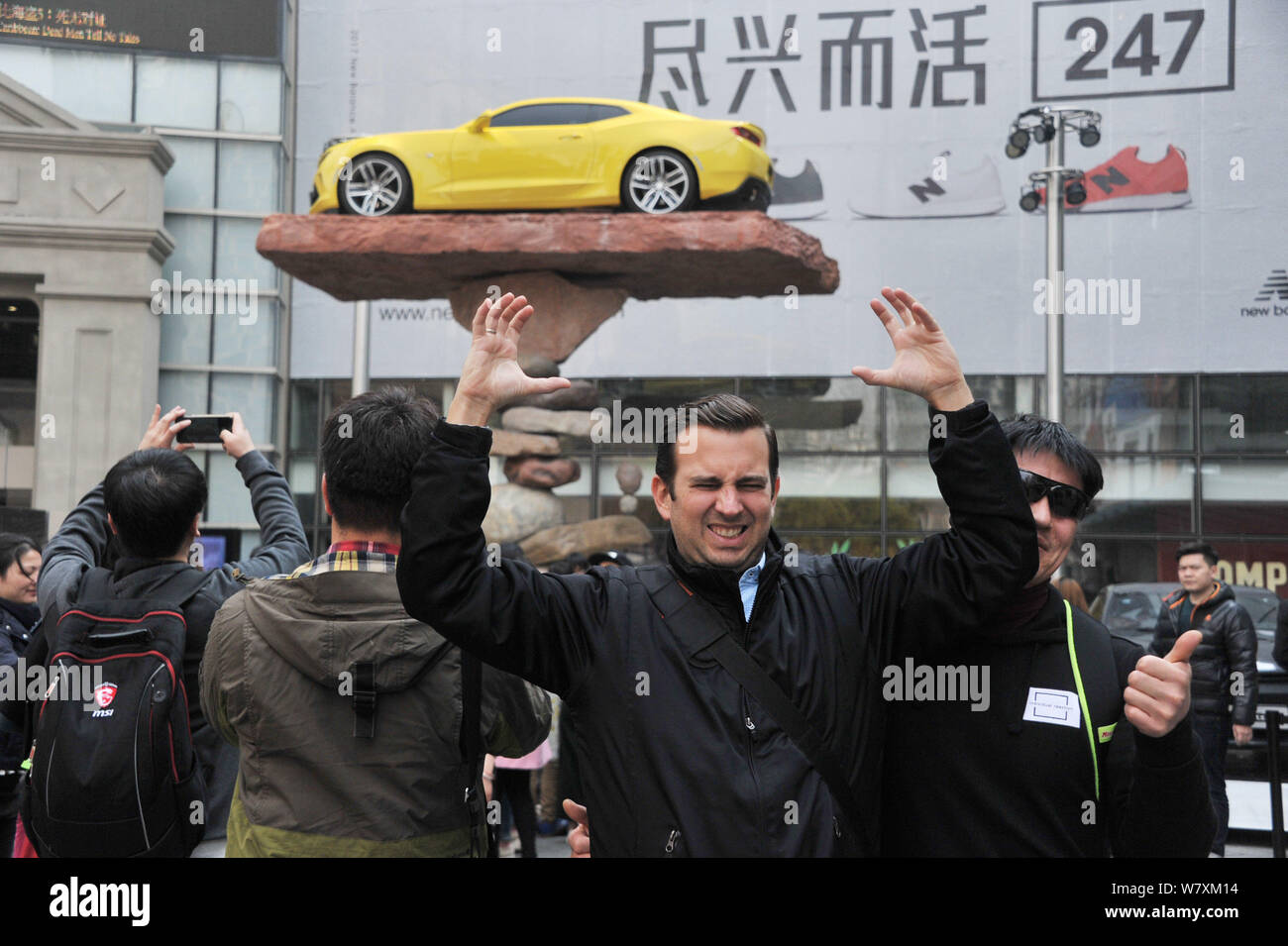 Un uomo pone di fronte a una installazione di arte di una vettura sportiva in equilibrio su una pila di rocce in Cina a Shanghai, 26 marzo 2017. Una vettura sportiva precariousl Foto Stock