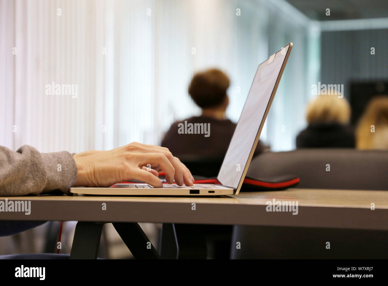 Donna che utilizza computer portatile in ufficio, mani femminili su una tastiera. Ragazza seduta con un notebook con telecamera chiusa in corrispondenza di una tabella su sfondo di persone Foto Stock