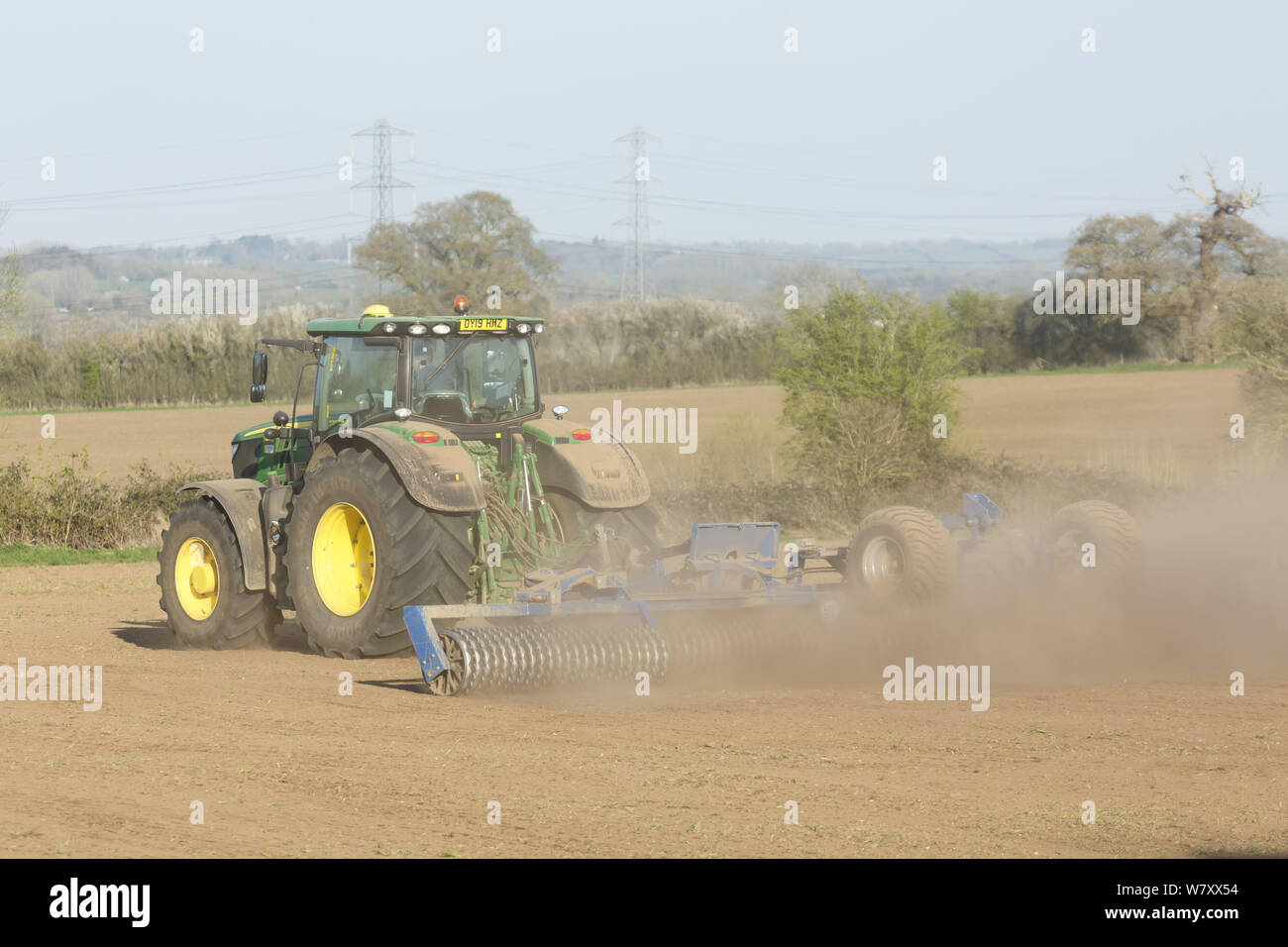 Buckingham, Regno Unito - 01 Aprile, 2019. Un trattore John Deere che coltiva la terra durante una siccità utilizzando un rullo di Cambridge o cultipacker. Buckingham, Regno Unito Foto Stock