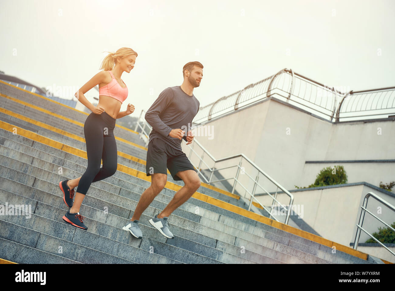 Allenamento mattutino insieme. Tutta la lunghezza di giovane coppia felice in abbigliamento sportivo che corre giù le scale mentre si esercita all'aperto. Concetto di sport. Stile di vita sano Foto Stock