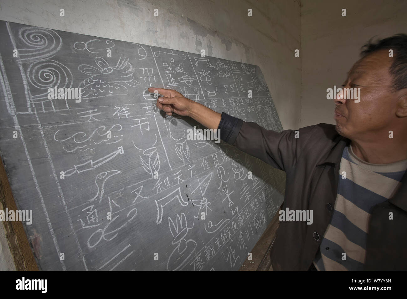 L'uomo puntando al pittogramma Naxi caratteri scritti sulla lavagna, Yunnan, Cina Foto Stock