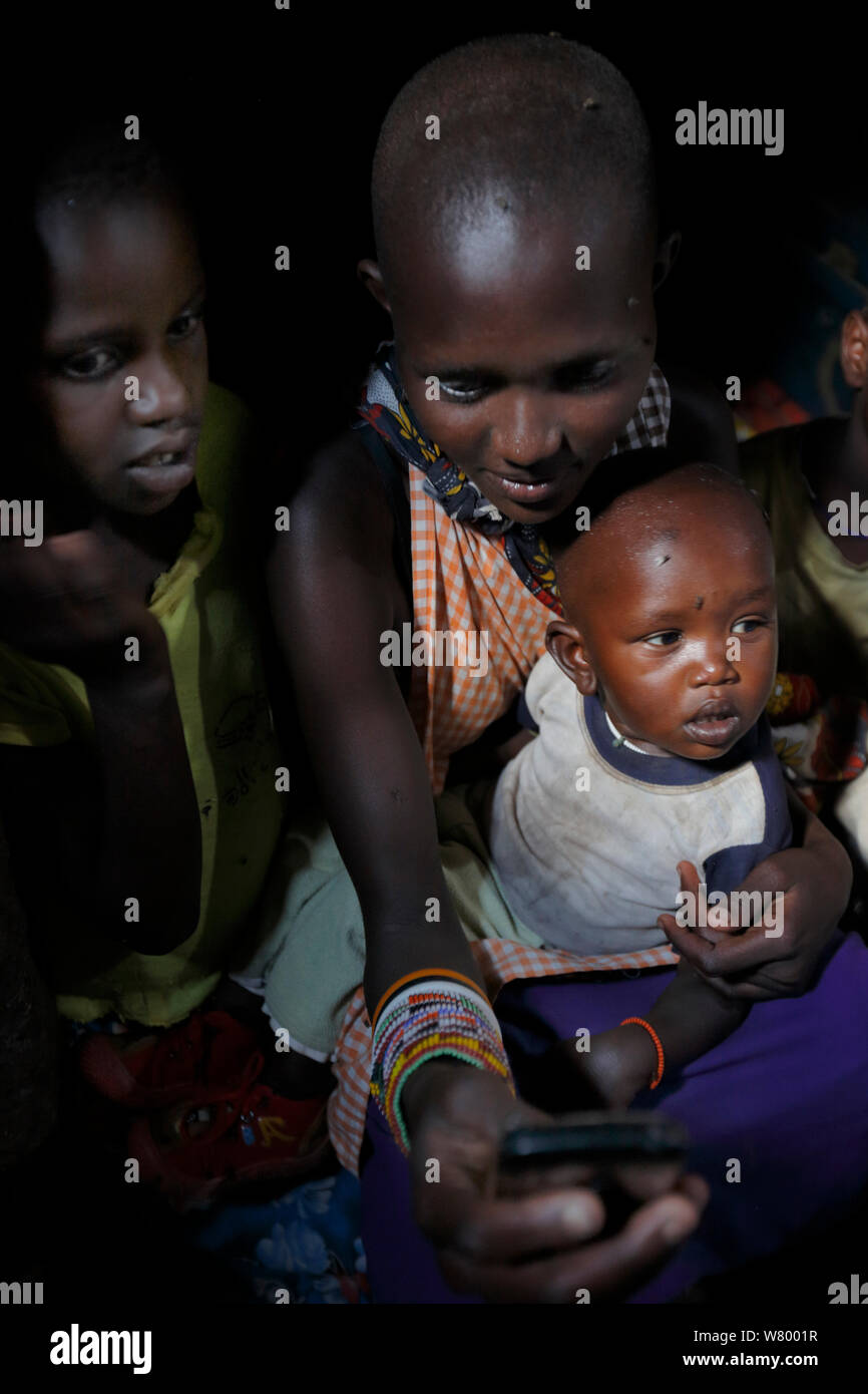 Masai famiglia nella capanna di argilla, ricarica cellulare utilizzando energia solare, Mara, Kenya. Marzo 2013. Foto Stock