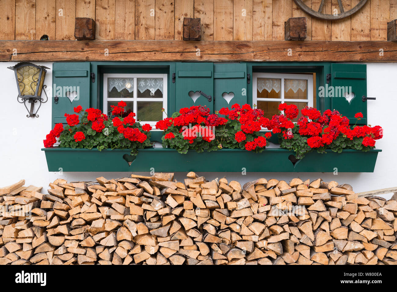 Fenster mit Geranien und Holzstapel in den Bayerischen Alpen Foto Stock