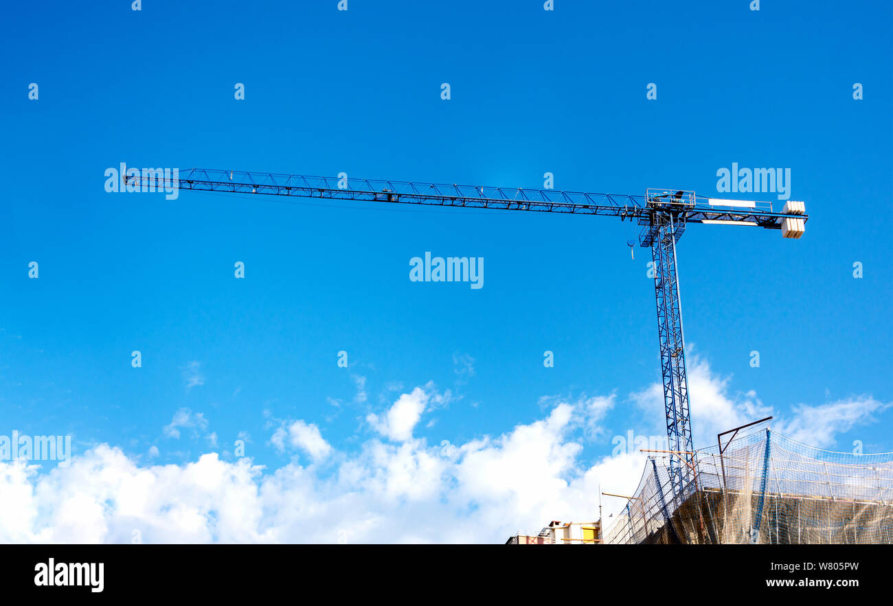 Una gru di sollevamento pesi su un sito di costruzione con un cielo blu e nuvole sullo sfondo. costruzione e ingegneria delle costruzioni. Foto Stock