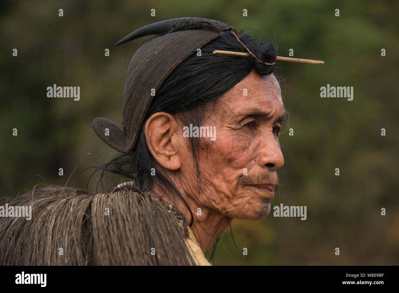 Apatani uomo con capelli tradizionale nodo fissato mediante un perno o Piidin Khotu e Lecha tradizionale sulla spalla e la canna da zucchero hat che comprende un becco hornbills. Tribù Apatani, Ziro Valle, foothills dell'Himalaya, Arunachal Pradesh.nord est dell India, novembre 2014. Foto Stock