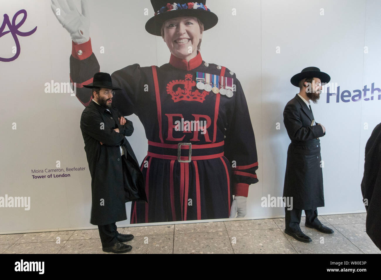 L'aeroporto di Heathrow, Londra, Regno Unito. Un gruppo di Ultra-Orthodox ("Haredi') ebreo pregano gli uomini in attesa di un volo. Una foto di Moira Cameron, beefeater (guardia cerimoniale) presso la Torre di Londra, in background. Foto Stock