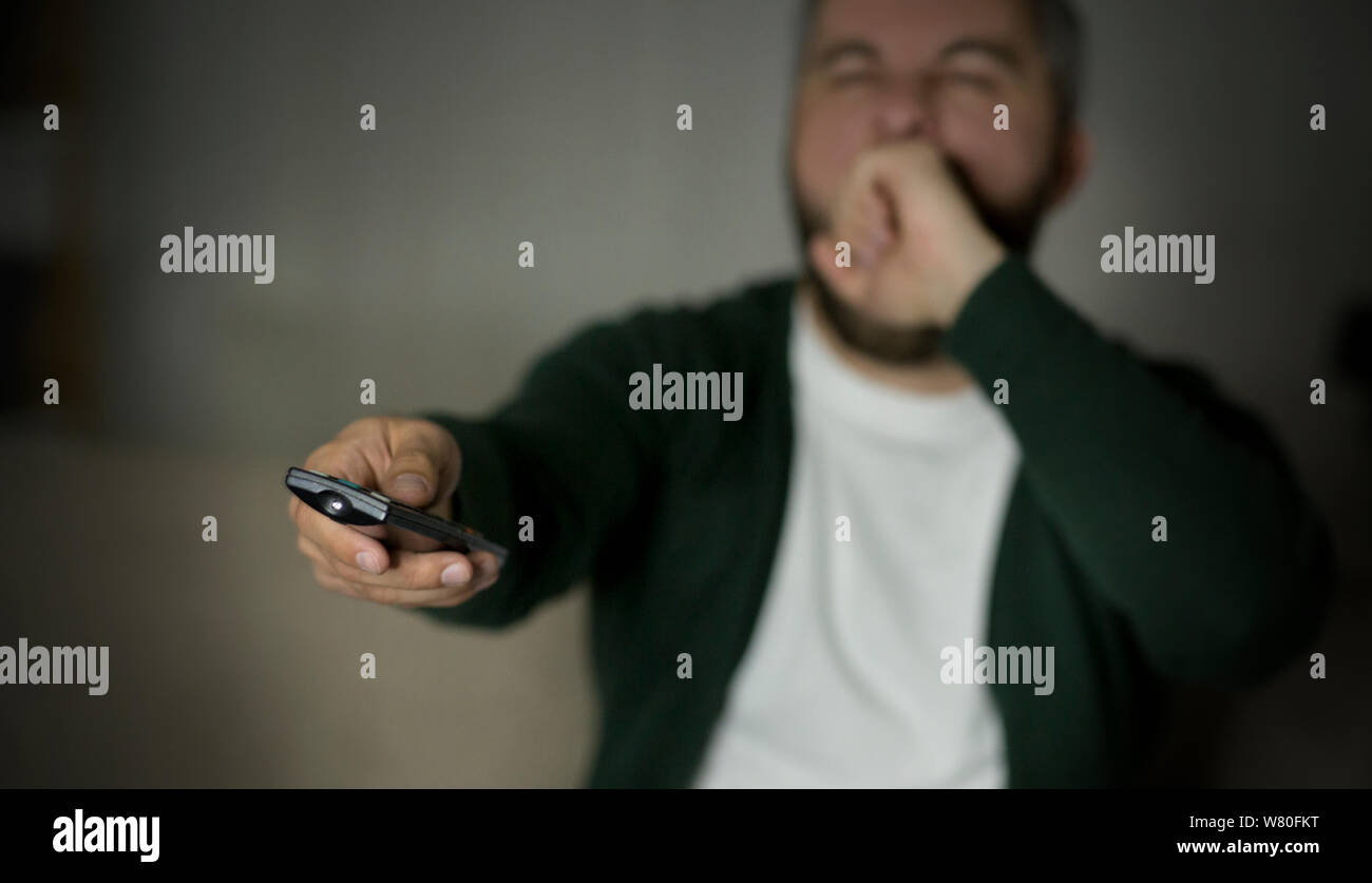 Sbadigliare uomo caucasico canali di commutazione sulla TV Foto Stock