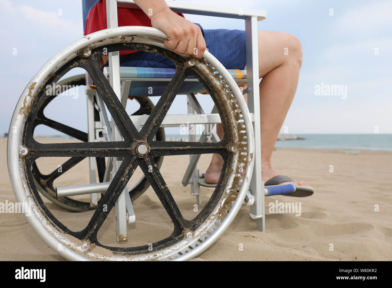 Dettaglio di una speciale sedia a rotelle con ruote di grande diametro per spostarsi sulla spiaggia sabbiosa del resort con un giovane uomo Foto Stock