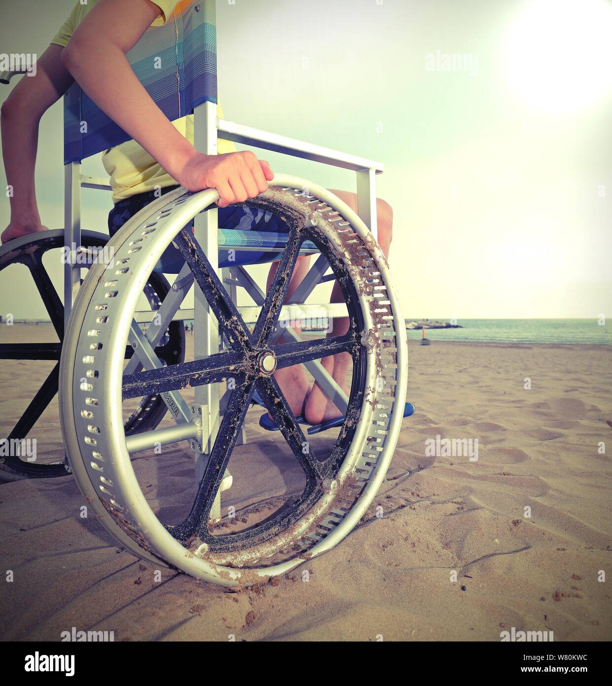 Dettaglio di una sedia a rotelle speciale con molto grandi ruote per spostarsi sulla spiaggia sabbiosa del resort con un ragazzo giovane Foto Stock