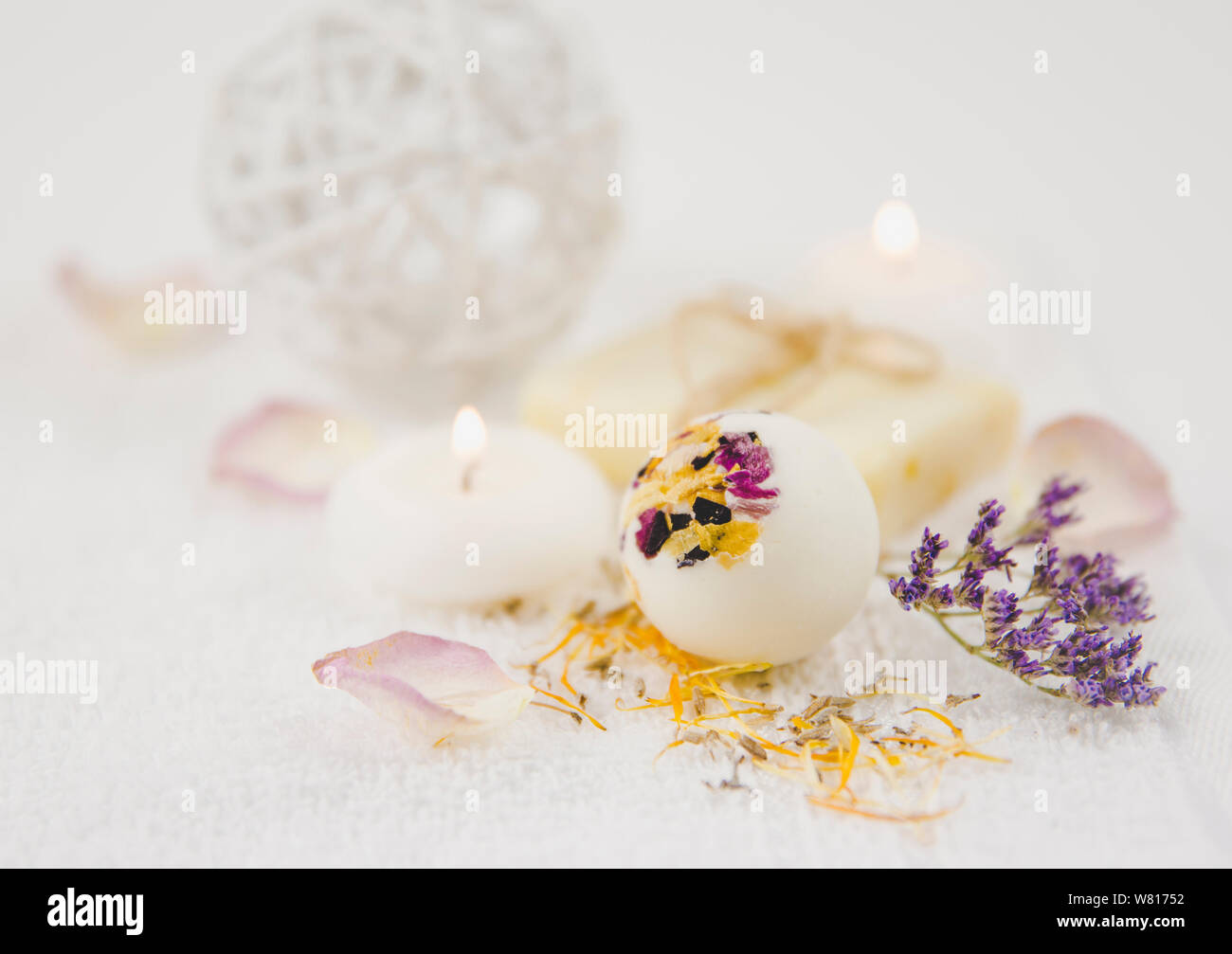 Bellissimo set con messa a fuoco selettiva su bianco cremoso idratante bagno piccola bomba a sfera con fiore secco petali di fiore, spa candele accese e flowe secco Foto Stock