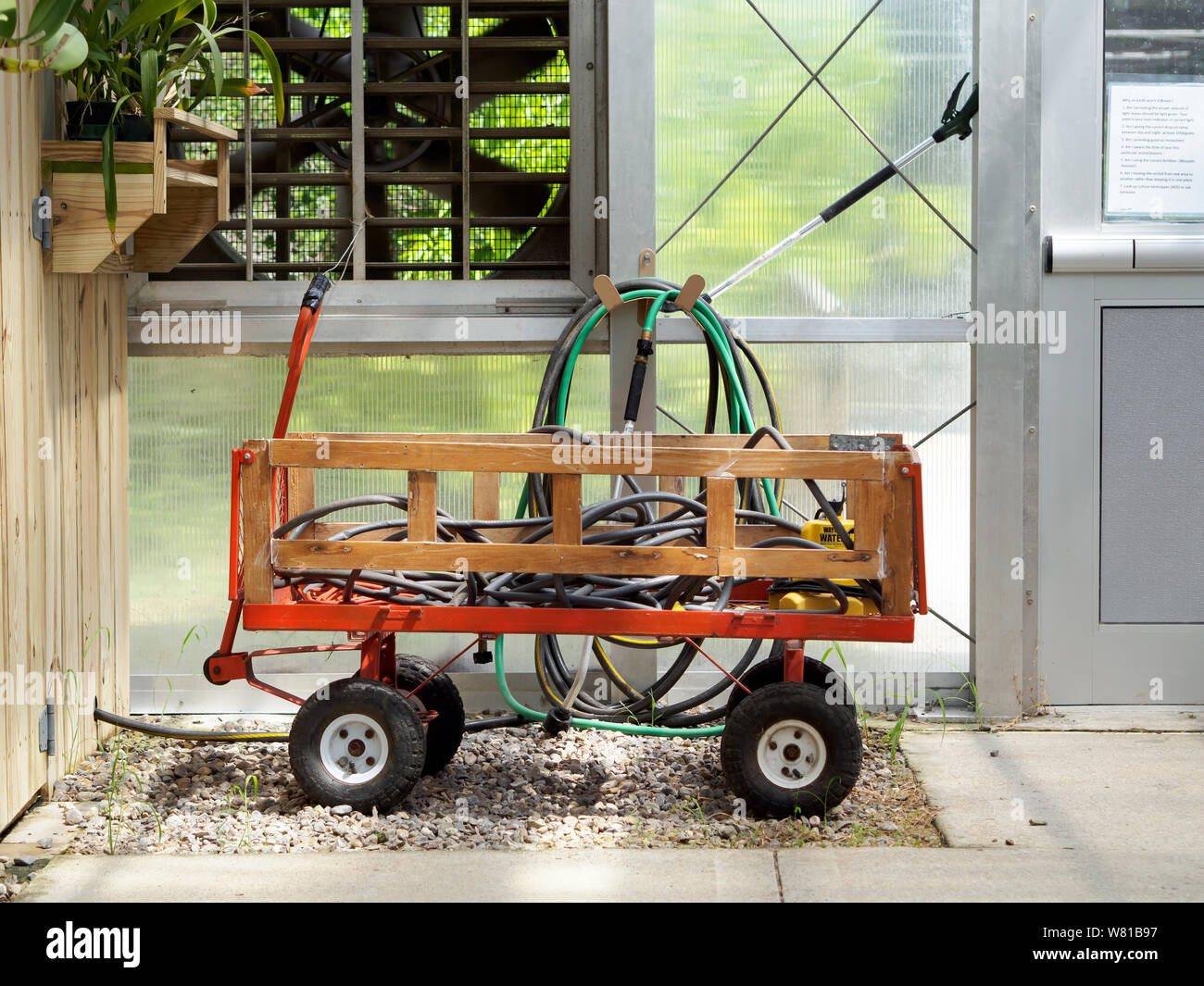 Carro carrello tubi flessibili di contenimento e attrezzature da giardino parcheggiato nella Serra delle Orchidee serra. Il Texas del sud i Giardini Botanici, il Corpus Christi, Texas USA. Foto Stock