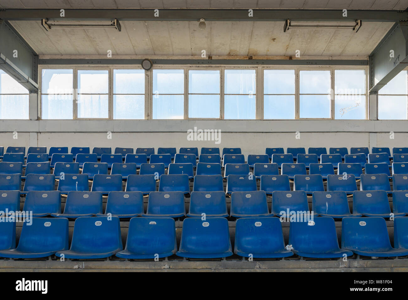 Vista frontale fila di plastica blu posti su terreni accidentati passo concreto piano nel vecchio vintage calcestruzzo sporco stadio strutturale senza persone. Foto Stock