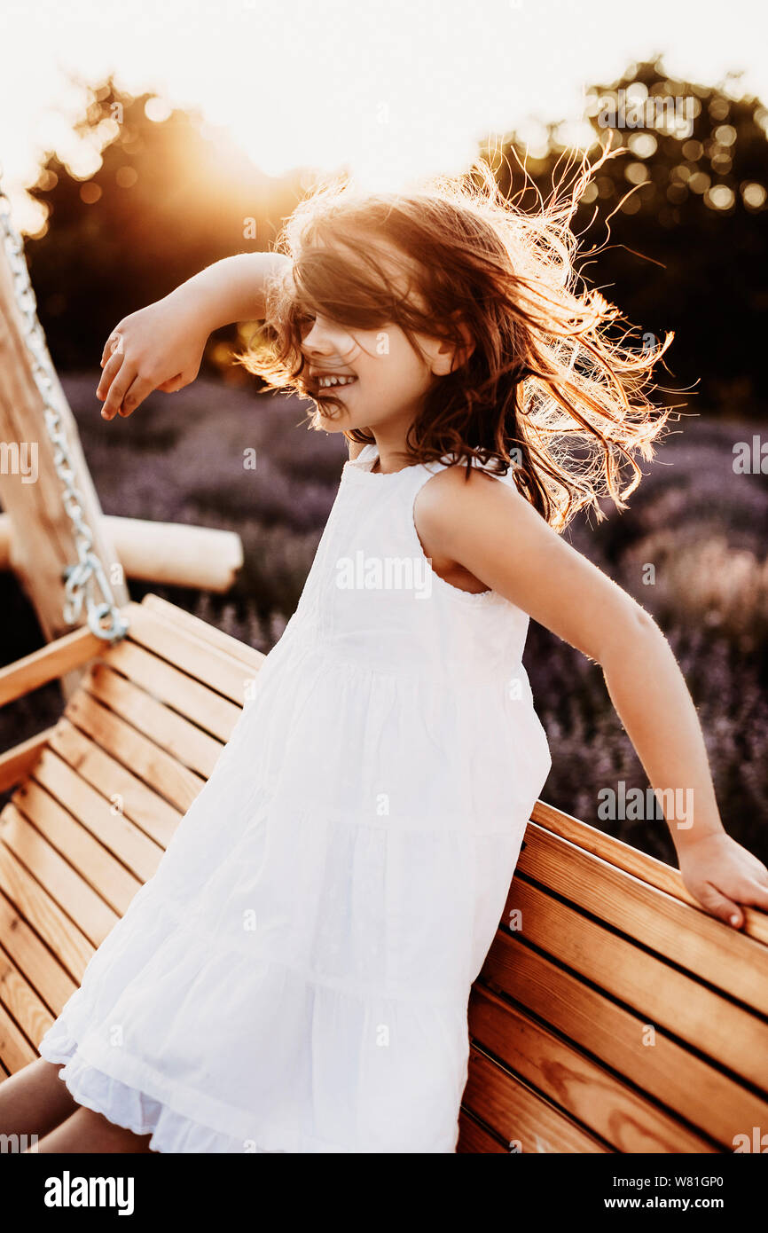 Ritratto di una bellissima bambina ballando nel vento contro il tramonto  sorridente vestito in abito bianco seduto su una oscillazione di legno in  un campo di lavanda Foto stock - Alamy