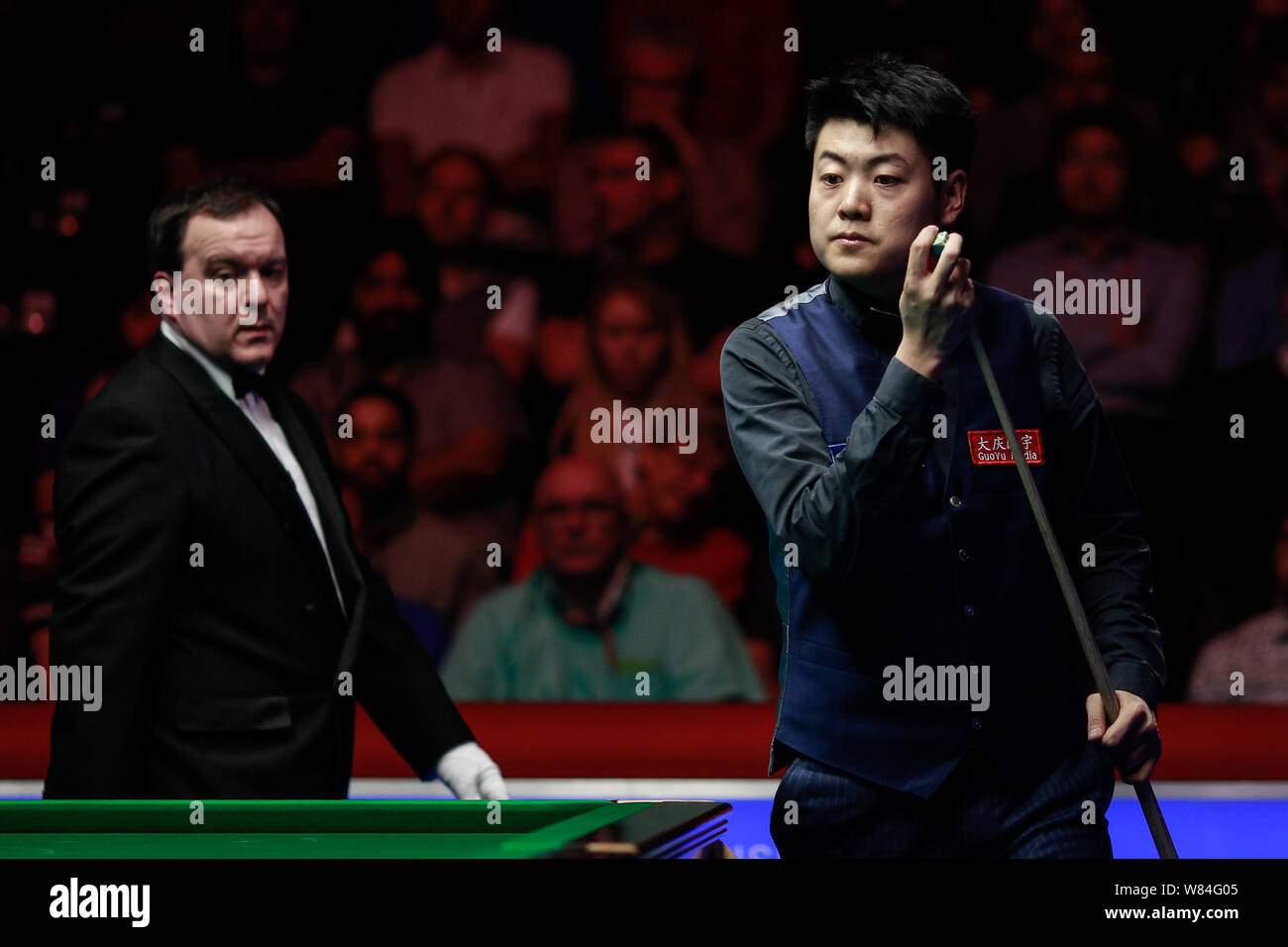 Liang Wenbo della Cina i gessi spunto come egli ritiene che un colpo contro Judd Trump di Inghilterra in loro corrispondenza finale durante l'inglese Open 2016 snooker tou Foto Stock