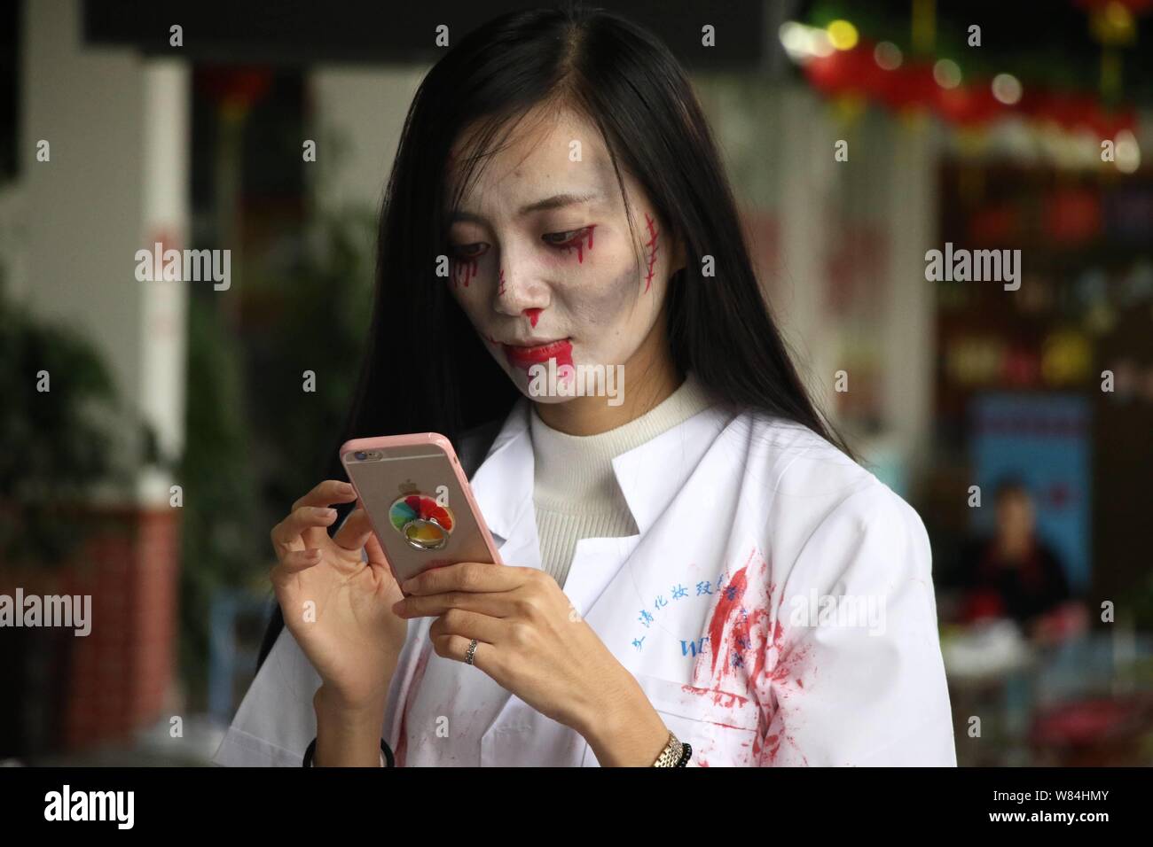 Una giovane donna con zombie trucco usa il suo smartphone durante un raduno per festeggiare Halloween presso un ristorante barbecue nella città Binzhou, est della Cina di Foto Stock