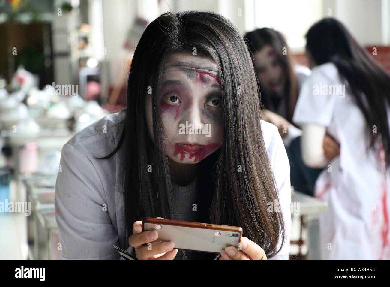 Una giovane donna con zombie trucco usa il suo smartphone durante un raduno per festeggiare Halloween presso un ristorante barbecue nella città Binzhou, est della Cina di Foto Stock