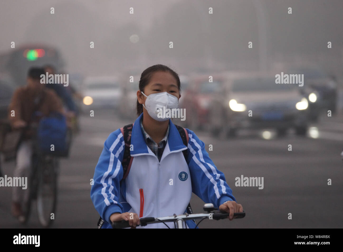 Una femmina di studenti cinesi che indossa una maschera facciale contro l'inquinamento atmosferico di cicli su strada di smog pesante di Tianjin, Cina, 19 ottobre 2016. Pechino ambi Foto Stock