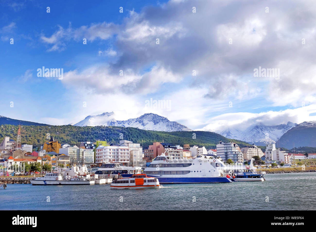 Vista delle navi nel porto di Ushuaia contro un paesaggio che mostra la città e arti marziali montagne coperte di neve e circondato da un cielo blu con whi Foto Stock