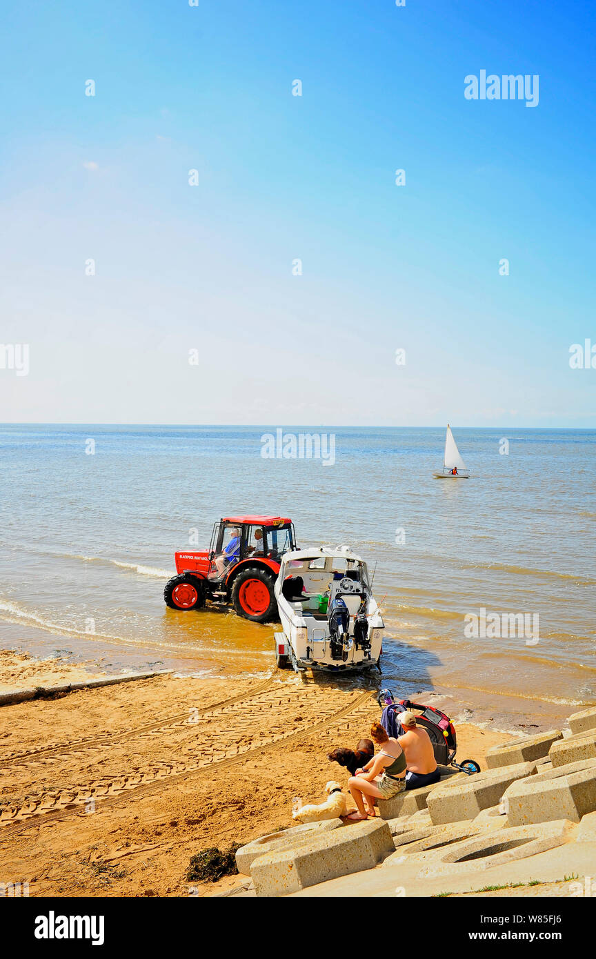 Red tractor pulling mare barca da pesca in mare a St Annes beach in una calda giornata estiva Foto Stock