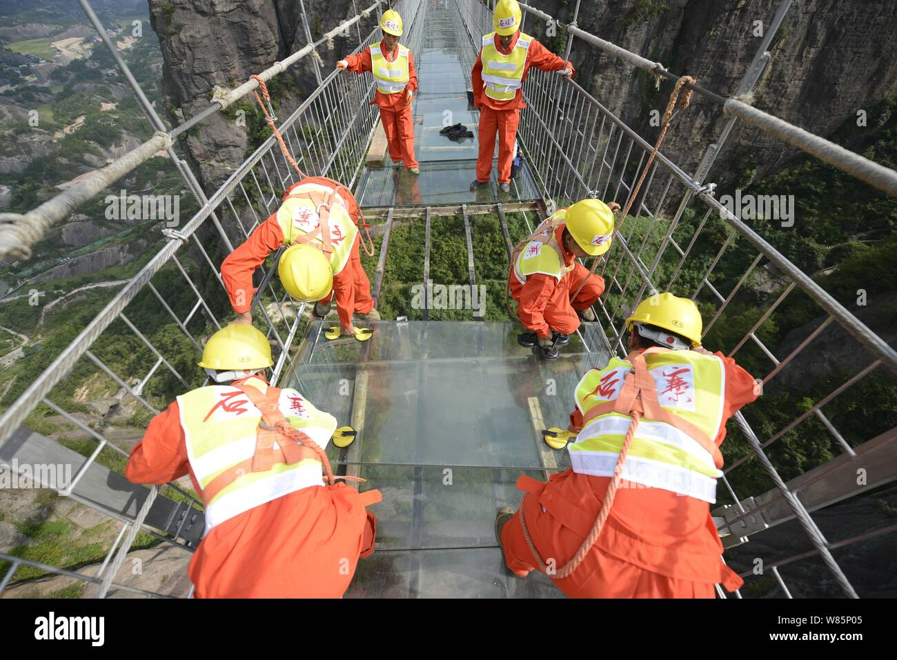 Lavoratori cinesi sostituire un graffiato pezzo di vetro con uno nuovo sul vetro con fondo di ponte di sospensione 180 metri sopra il livello del suolo al Shiniuzha Foto Stock