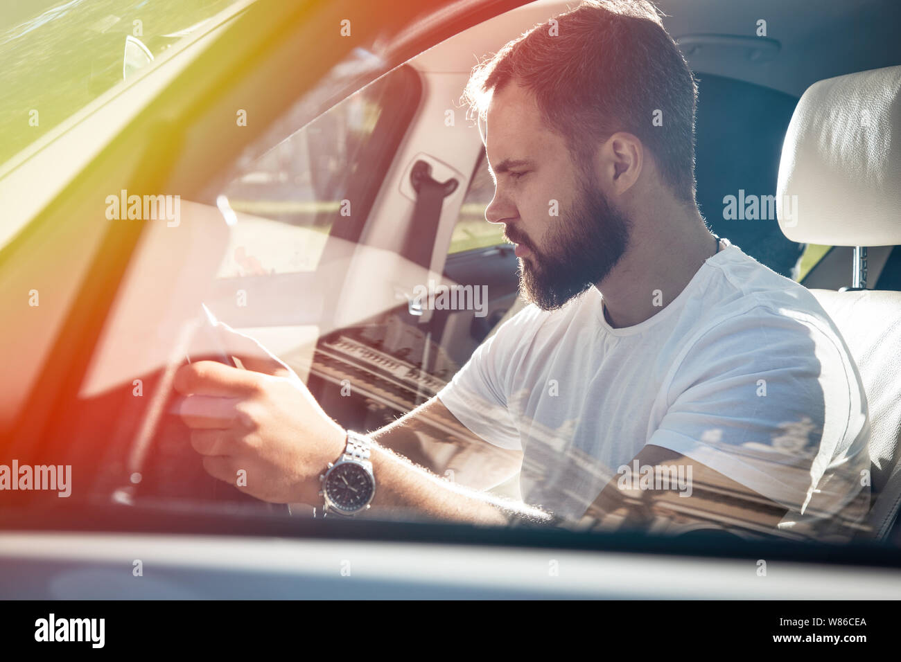 L'uomo dietro la ruota inizia una vettura bianca, abbigliamento casual, metallo orologi da polso, pensieroso look. Foto Stock