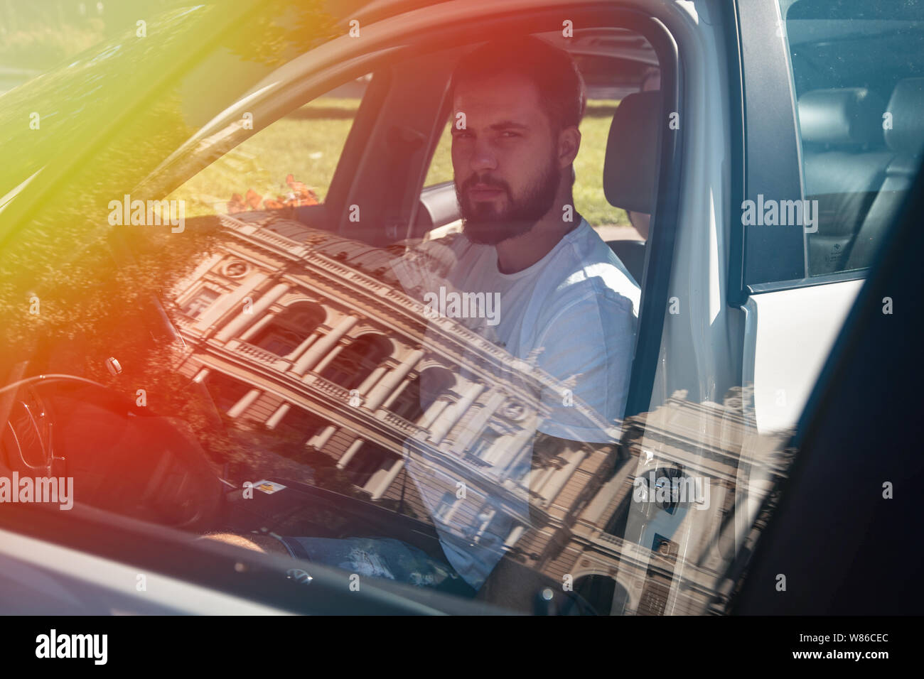 L'uomo dietro la ruota inizia una vettura bianca, abbigliamento casual, metallo orologi da polso, pensieroso look. Foto Stock