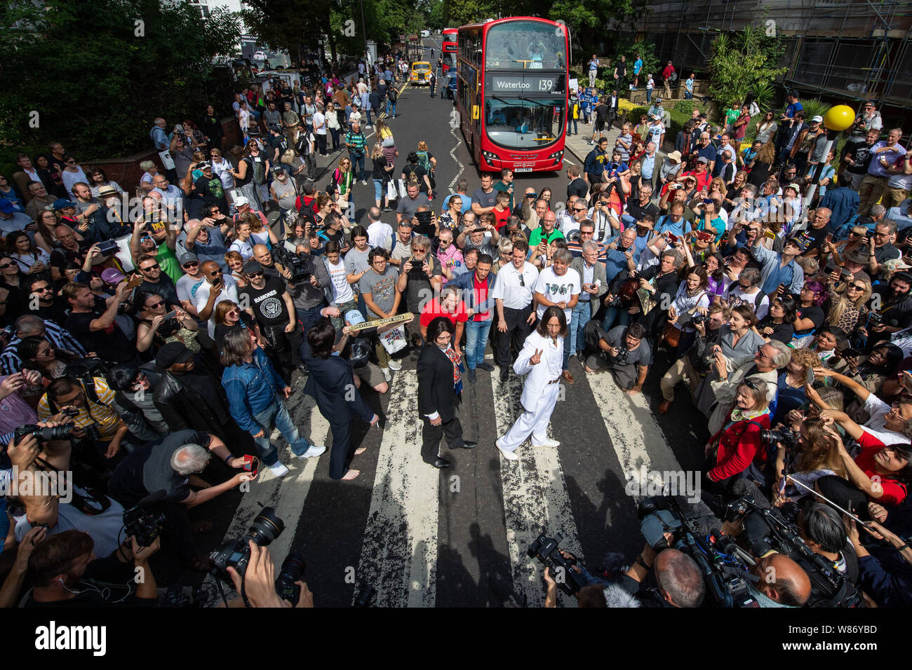 Beatles lookalike banda "Fab Four" unisce i fan dei Beatles come essi a piedi attraverso la Abbey Road attraversando a Londra in occasione del cinquantesimo anniversario della band di farlo per il loro album iconica coprono il 8 agosto 1969. Foto Stock