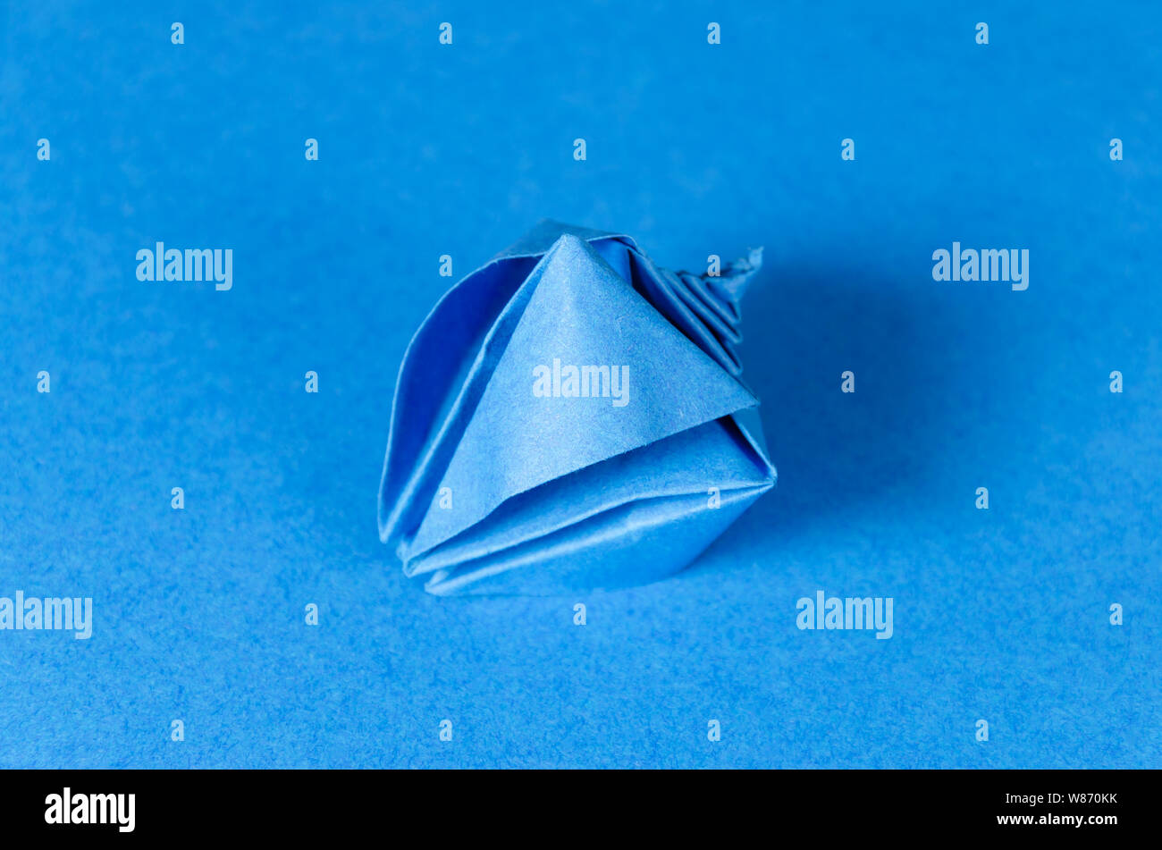 Blue origami seashell su sfondo blu. Arte giapponese di piegatura della carta. Quadrato piatto foglio di carta trasferiti nella scultura finito. Foto Stock