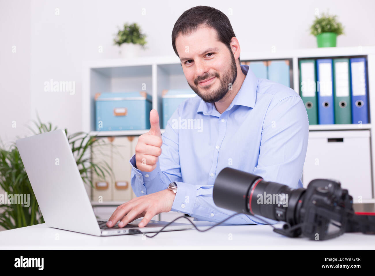 Barbuto fotografo presso il suo ufficio con il laptop e la fotocamera. Foto Stock