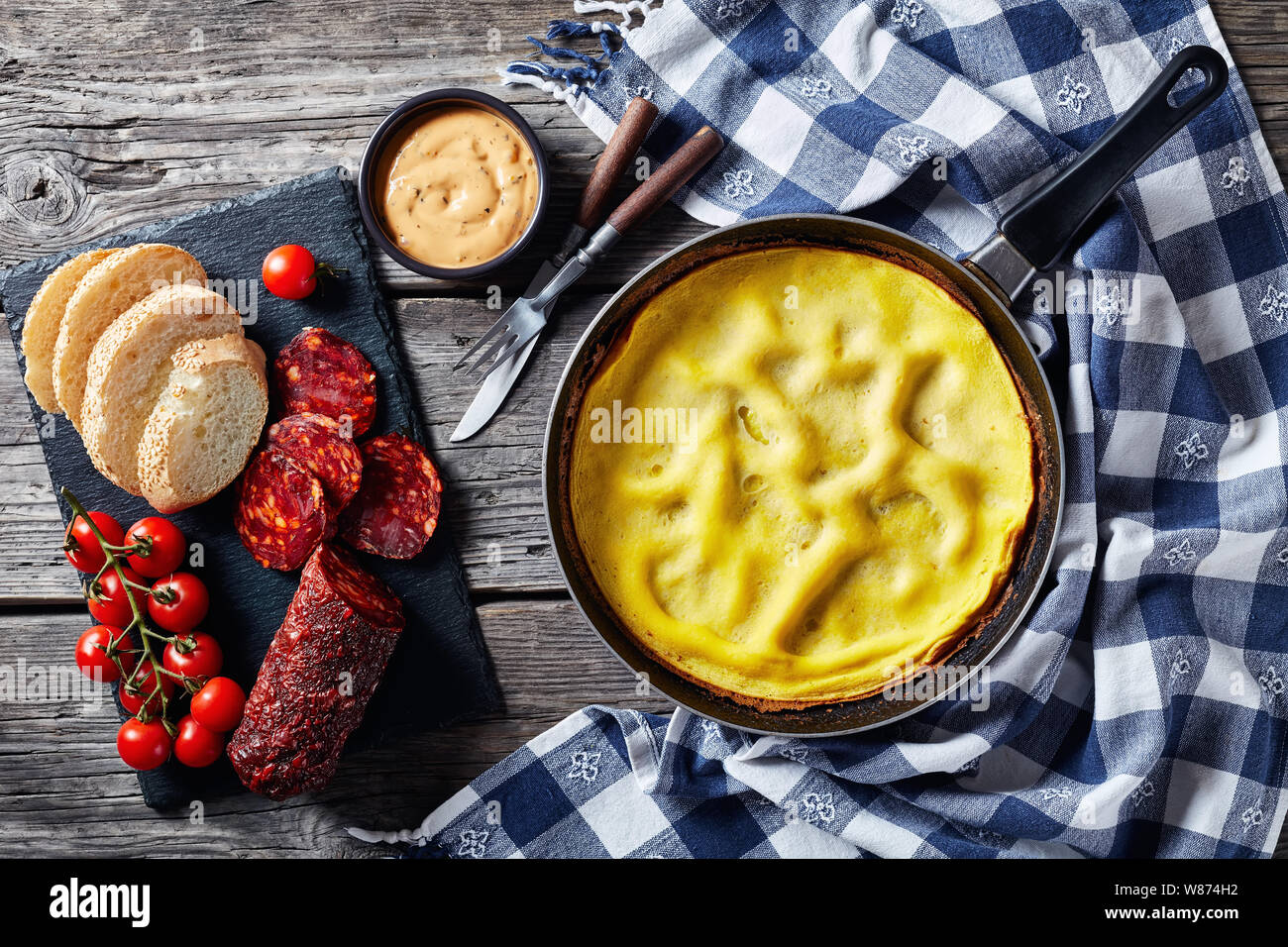 Frittata di caldo in una padella, affettato chorizo, pane e pomodori su un scheda di ardesia, vista da sopra, piatto laici, spazio di copia Foto Stock