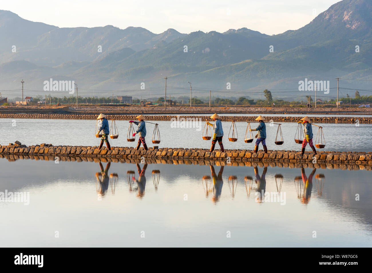 Donna lavoratori portando cesti di appena raccolto il sale sulle loro spalle in Hon Khoi campo sale di sunrise, Nha Trang Provincia, Vietnam Foto Stock