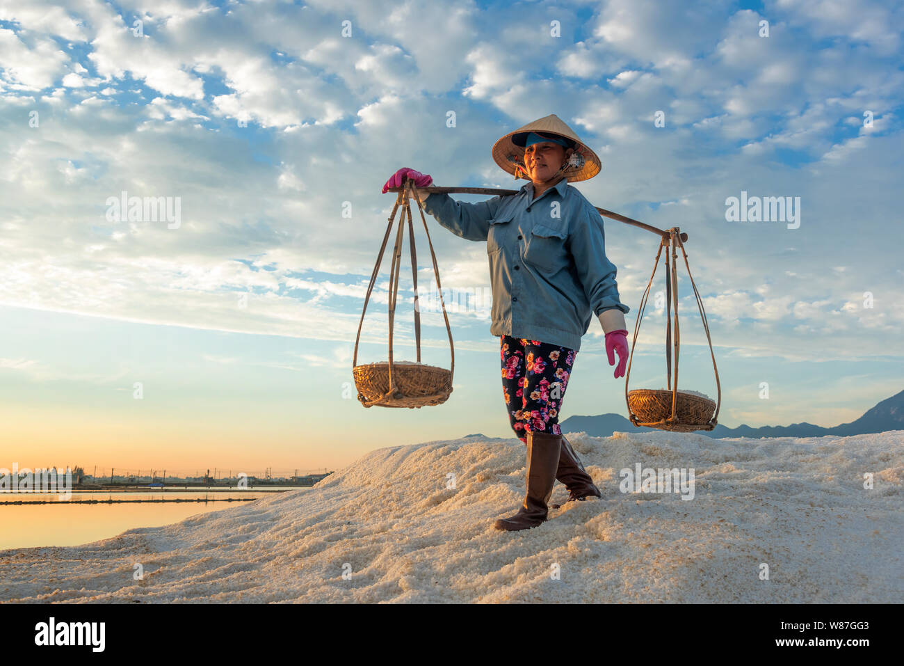 La donna lavora duramente portando pesanti ceste di sale sulle loro spalle la mattina presto a Hon Khoi campo sale, Nha Trang Provincia, Vietnam Foto Stock