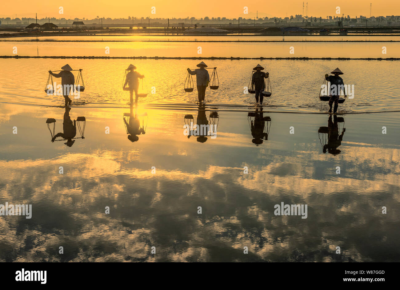 Donna lavoratori portando cesti di appena raccolto il sale sulle loro spalle in Hon Khoi campo sale di sunrise, Nha Trang Provincia, Vietnam Foto Stock