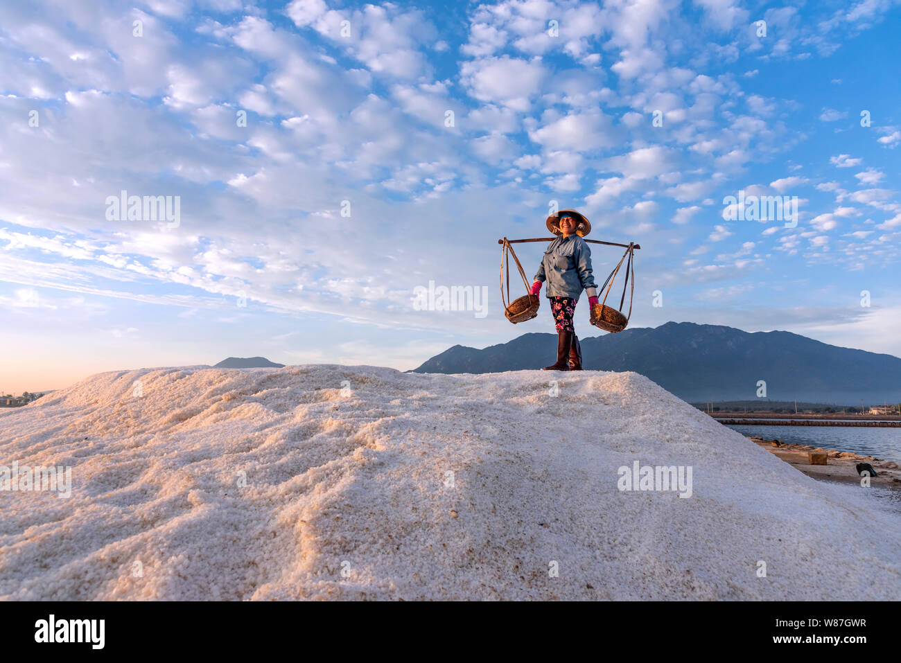 La donna lavora duramente portando pesanti ceste di sale sulle loro spalle la mattina presto a Hon Khoi campo sale, Nha Trang Provincia, Vietnam Foto Stock