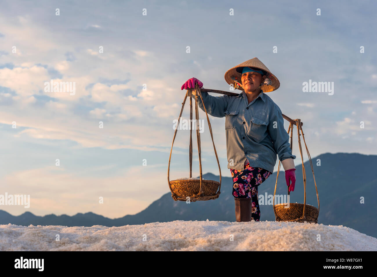 La donna lavora duramente portando pesanti ceste di sale sulle loro spalle la mattina presto a Hon Khoi campo sale, Nha Trang Provincia, Vietnam Foto Stock