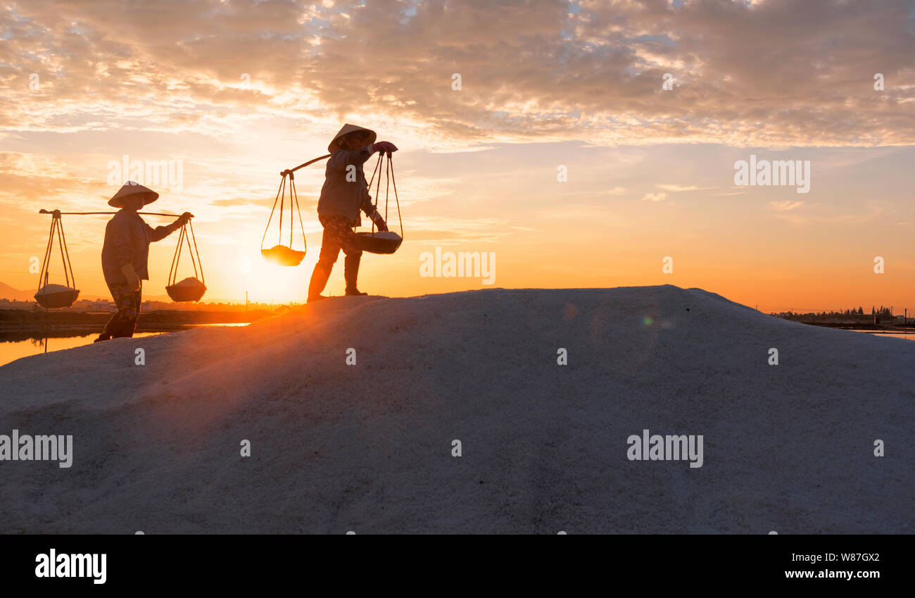 La donna lavora duramente portando pesanti ceste di sale sulle loro spalle la mattina presto a Hon Khoi campo sale, Nha Trang Provincia, Vietnam Foto Stock