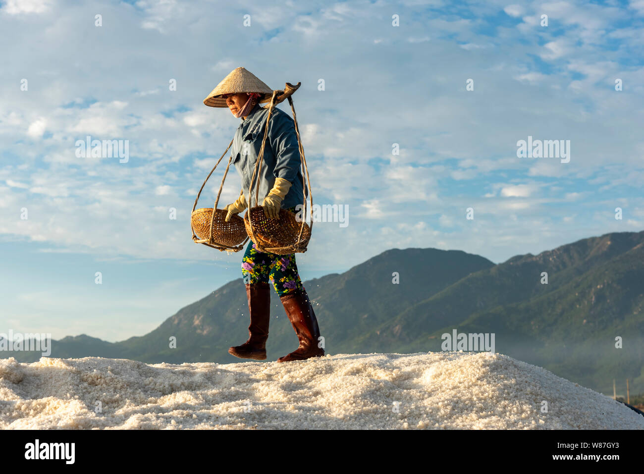 La donna lavora duramente portando pesanti ceste di sale sulle loro spalle la mattina presto a Hon Khoi campo sale, Nha Trang Provincia, Vietnam Foto Stock