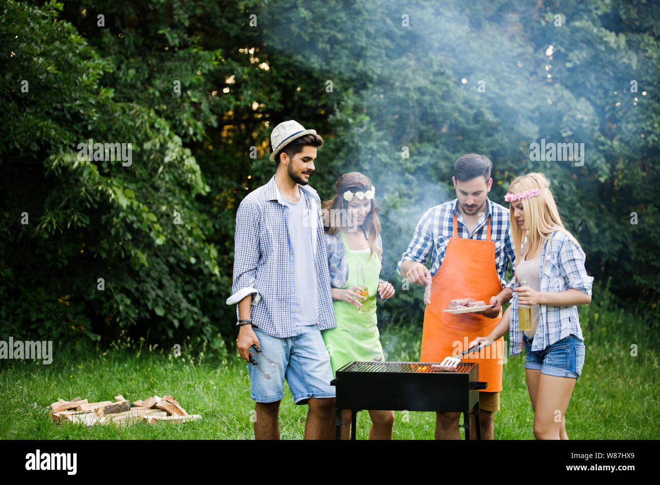 Gruppo di persone felici intorno permanente grill, chat, bere e mangiare. Foto Stock