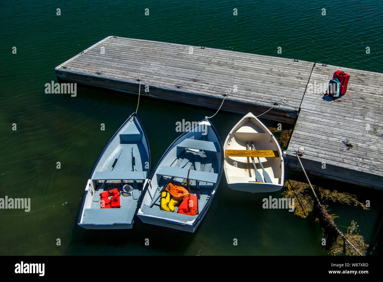 Tre piccole imbarcazioni a remi ormeggiate ad un dock grigio inferiore nella baia di Muscongus vicino a Bremen, Maine, Stati Uniti d'America. Foto Stock