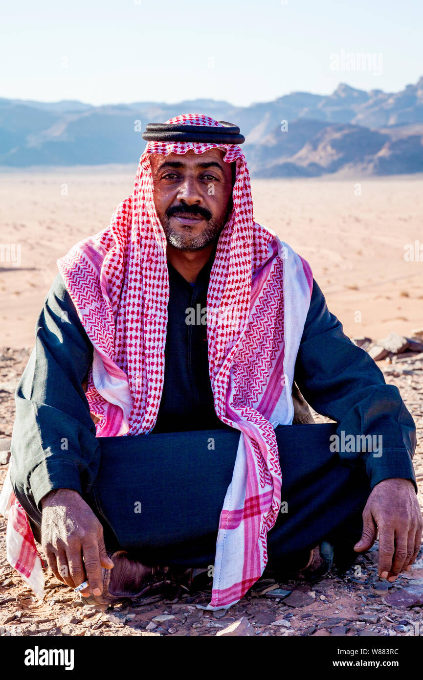 Un beduino uomo si siede sullo sfondo del deserto giordano a Wadi Rum o a valle della luna Foto Stock