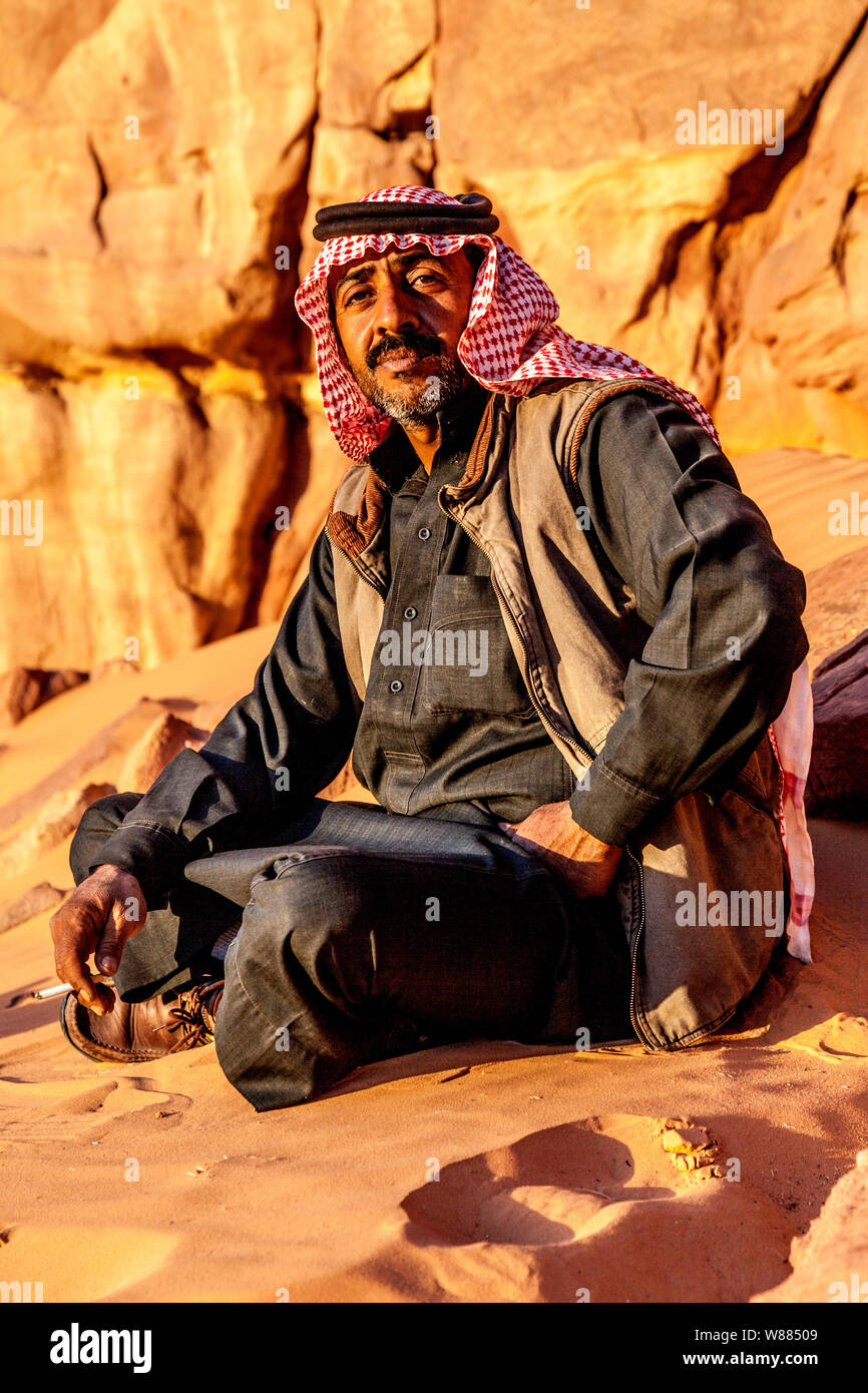 Un beduino uomo si siede sullo sfondo del deserto giordano a Wadi Rum o a valle della luna Foto Stock