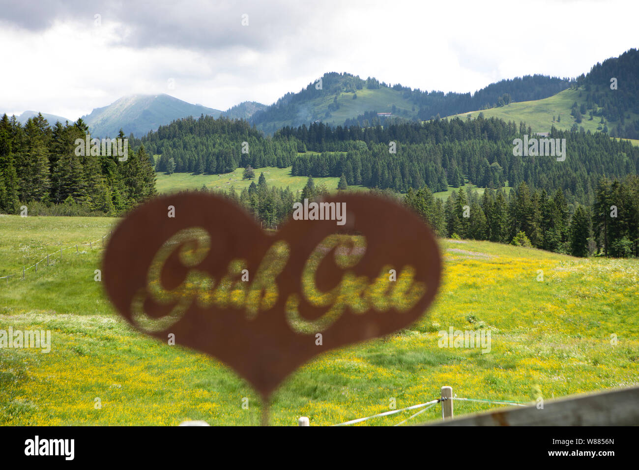 Rusty segno di benvenuto con il tedesco lettere a forma di cuore in un pascolo alpino Foto Stock