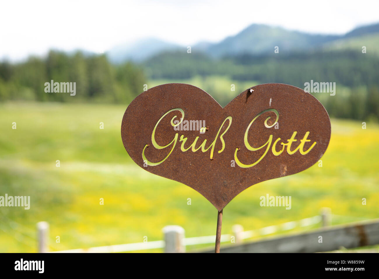 Rusty segno di benvenuto con il tedesco lettere a forma di cuore in un pascolo alpino Foto Stock