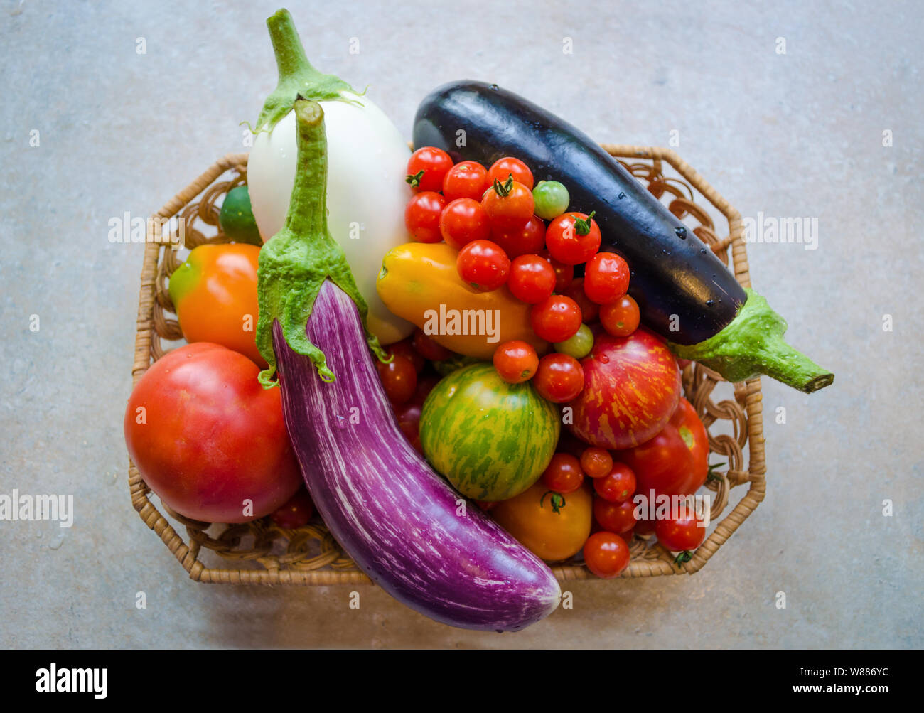 Un cesto pieno di fresche e mature verdure organiche - bianco e viola melanzane, pomodori arancione, pomodorini e pomodori rossi Foto Stock