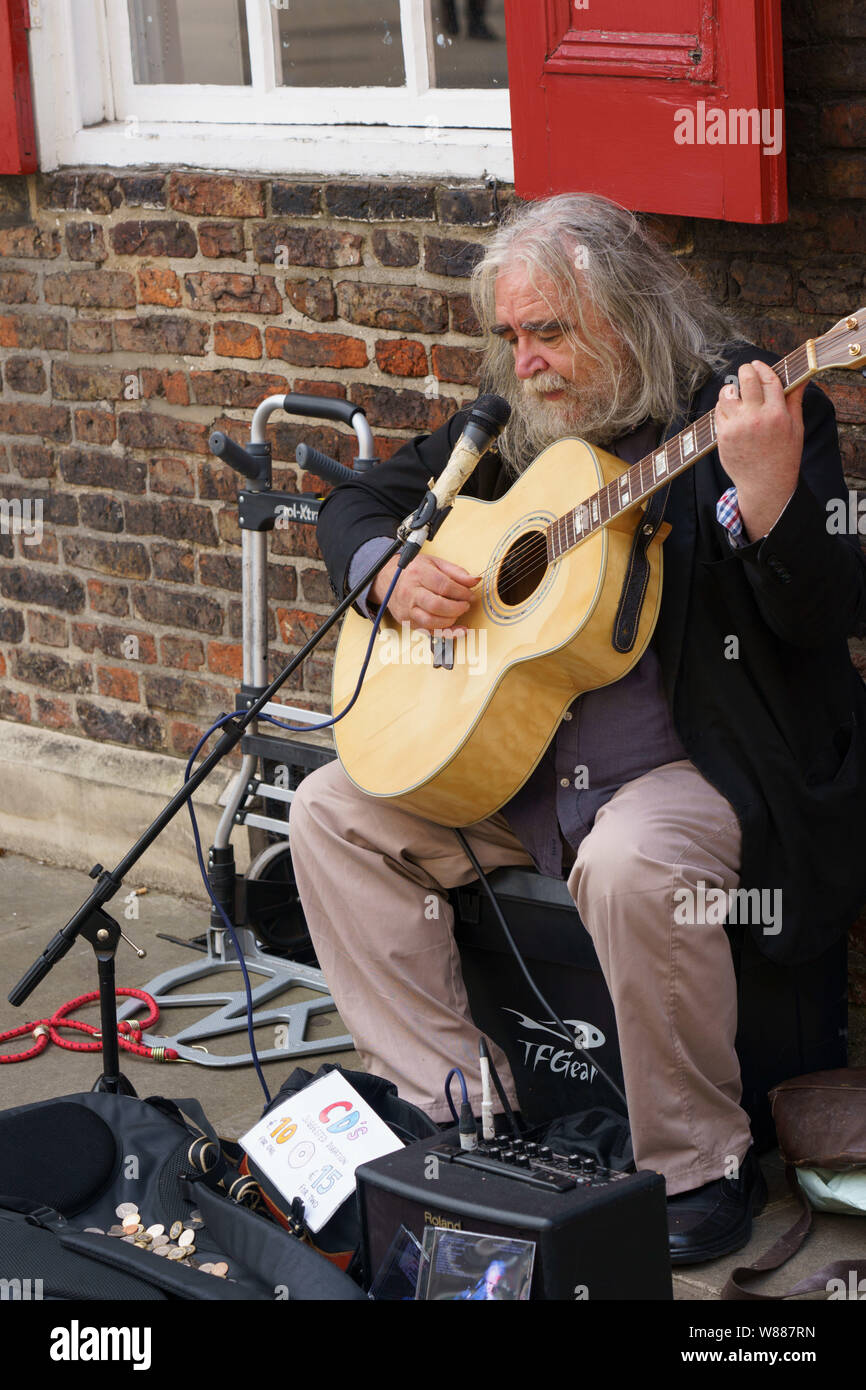 Uomo dai capelli lunghi e grigi che canta e suona la chitarra acustica in una strada a York, North Yorkshire, Inghilterra, Regno Unito. Foto Stock