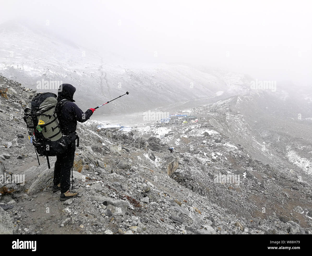 Tourist mostra la direzione del campo base Everest, foggy meteo e nevica; multicolore preghiera tibetano bandiere con iscrizioni sacre attaccata Foto Stock