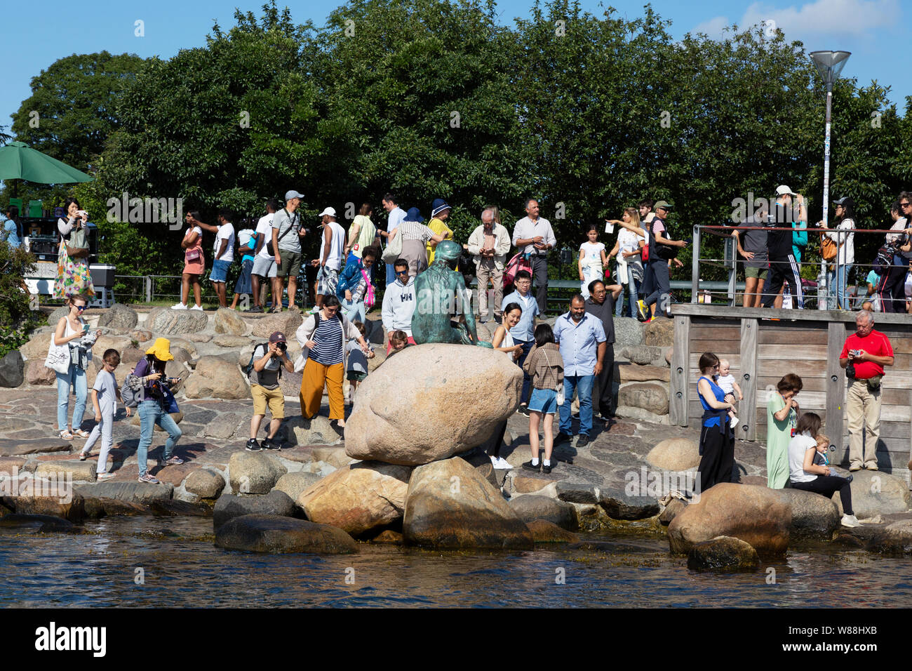 Viaggi di Copenaghen; vista posteriore della statua della Sirenetta e turisti, Copenhagen DANIMARCA Europa Foto Stock