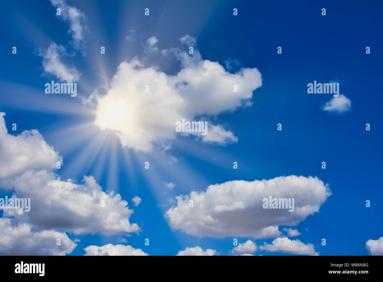 Sole splende luminosa attraverso nuvole bianche su un cielo blu, con raggi di sole Foto Stock